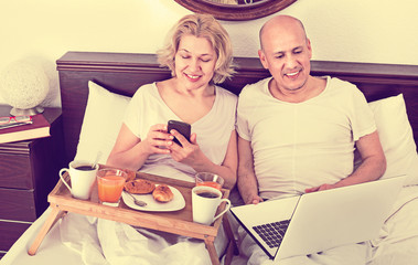 Mature positive couple reading news from notebook