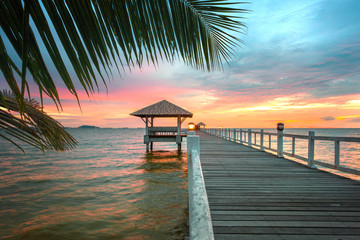 wooden bridge walkway straight destination laying to the sunset at the sea, with a shadow of the three covering on the bridge