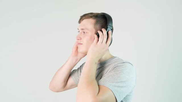 Young man puts on his headphones and listening to music on white background