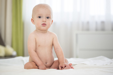 Cute naked baby boy sitting on bed