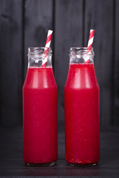 Raspberries juice in a two glass bottle on black wooden background, close up