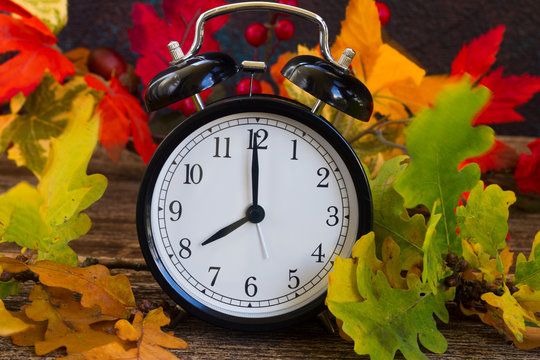 Autumn time - fall multicolored leaves with alarm clock close up