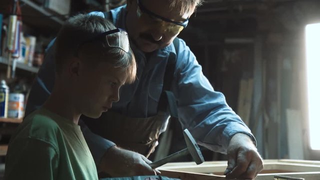 Adult carpenter drilling window and teaching grandson in workshop.