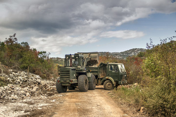 Obraz premium Montenegro - A wheel loader and a truck clear landslide of rocks from the mountain road