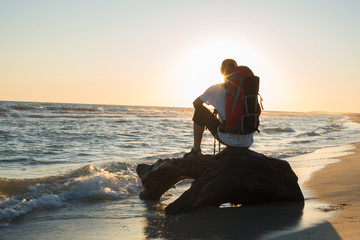 Man traveler with backpack sits in the surf