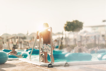 The child stands with his back holding the bumper at the pool talking to his mother, happy that...