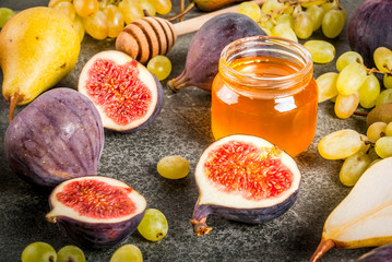 Snacks, dietary vegan desserts. Autumn fruits (figs, pears, grapes) with honey on a black stone table. Copy space top  view