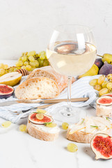 Sandwiches with ricotta or cream cheese, ciabatta, fresh figs, pears, grape, walnuts and honey on white marble table table, with wine glass copy space