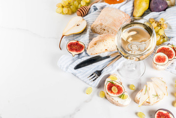 Sandwiches with ricotta or cream cheese, ciabatta, fresh figs, pears, grape, walnuts and honey on white marble table table, with wine glass copy space top view