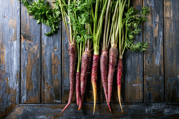 Bundle of raw organic purple carrot with green top haulm over old wooden plank background. Top view with copy space. Food background.