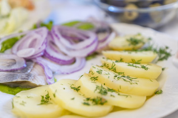 close up of sliced boiled potato, red onion and herring on a white plate