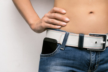 Mobile phone in jeans pocket of a girl person with hand on the waist.