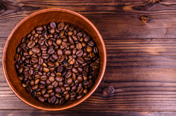 Roasted coffee beans in bowl on wooden table. Top view