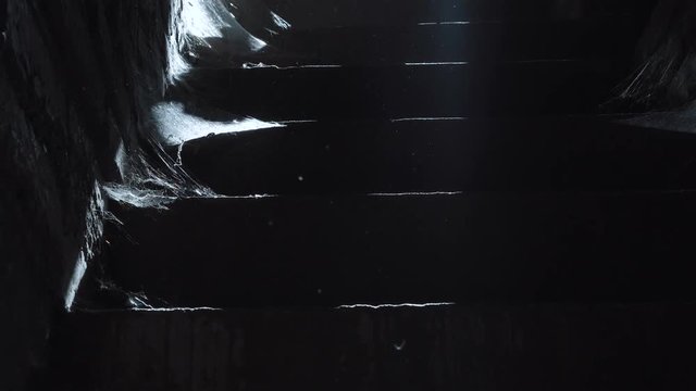 A view of the dusty staircase with cobwebs, silhouette of unrecognizable man in boots goes down the stairs.