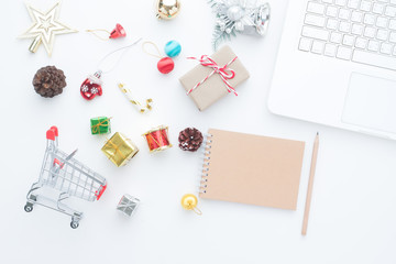 Shopping cart and Christmas decorations on white background with laptop computer and empty notebook, Top view