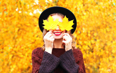 Autumn portrait smiling woman hides her eyes maple yellow leaves in black hat