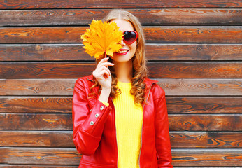 Cheerful woman hides half face autumn yellow maple leaves over wooden background