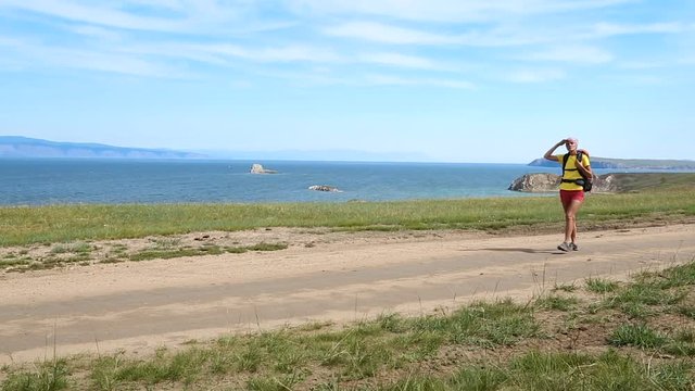 Hiking woman with backpack trekking along blue lake Baikal. Caucasian girl living active lifestyle