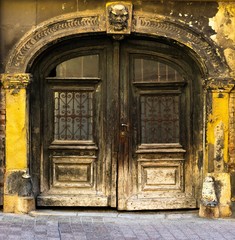 View of an old arched beautiful carved wooden front door or gate on an old building with damaged yellow facade