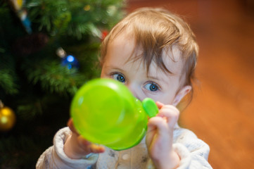 baby drinks from a feeder cup of green next to the Christmas tree