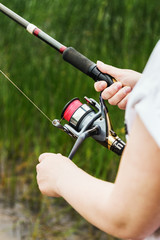 female hands holding a fishing rod and twist the handle of the fishing reel. Shallow depth of field, soft focus