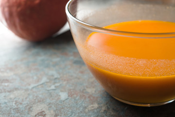 Pumpkin soup in a glass bowl and pumpkin on a blue stone