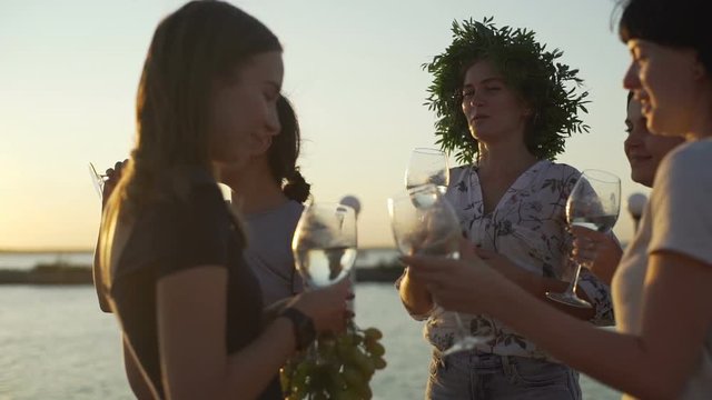 Beautiful girls clink wine glasses at pier seaside sunset rapid slow motion