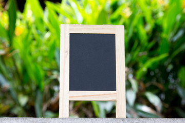 Black board with easel stand on green leaf background