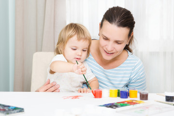 child girl and mother drawing  with colored inks paint  together. Young mother teaching her toddler  daughter to draw.