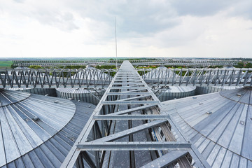 Fototapeta premium Agricultural Silos. Building Exterior. Storage and drying of grains, wheat, corn, soy, sunflower against the blue sky with white clouds