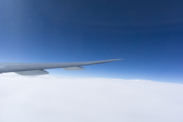 Airplane wing above cloud under clear blue sky.