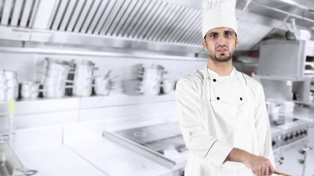 Male Caucasian chef looks angry in the kitchen, scolding at the camera while holding a wooden spatula and wearing uniform