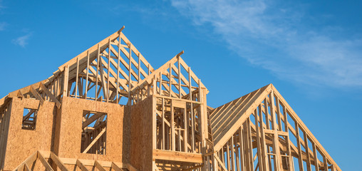 Close-up of gables roof on stick built home under construction and blue sky in Humble, Texas, USA. New build roof with wooden truss, post and beam framework. Timber frame house, real estate. Panorama