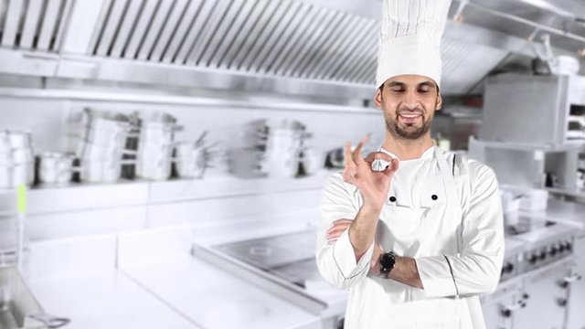 Handsome Caucasian chef showing OK sign while smiling and wearing uniform in the kitchen