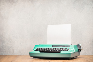 Retro old mint green typewriter with paper blank on wooden table front concrete wall background....