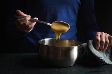 Spoon in hand with base sauce roux on blue background side view