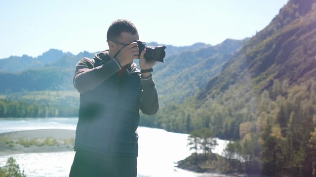 Young man in sunglasses taking picture with professional camera in the mountain on nature. 3840x2160
