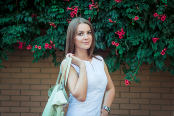 Portrait of beautiful young smiling woman, wearing elegant white dress, holding  leather hand bag, ...