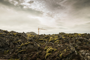 Lifting construction crane among the rocky terrain covered with lava and moss. Iceland. Construction in hard-to-reach places.
