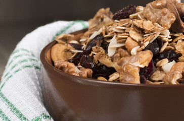 Homemade granola with honey, oatmeal, cashew nut, almond, pistachio, raisin and cranberry in clay bowl,glass with milk on wood dark table,