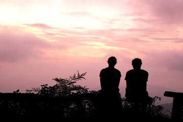 Fototapeta na wymiar Silhouette Man and woman sitting watch the evening sky at purple sunset