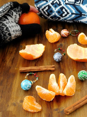 Mandarins, little Christmas balls, knitted sweater and a hand in a mitten is holding a mandarin on a wooden table