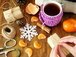 Mandarins, hot tea and present boxes on a wooden table. Process of wrapping the gifts
