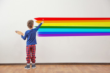Cute little boy painting on wall in empty room