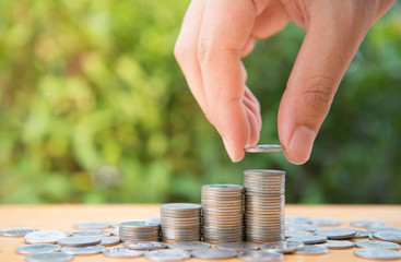 Human hand is putting coin to growing coin stack with nature background for saving money concept