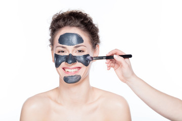 Young woman having a black charcol mask applied on her skin.