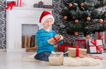 Cute boy in santa hat unwrapping christmas presents