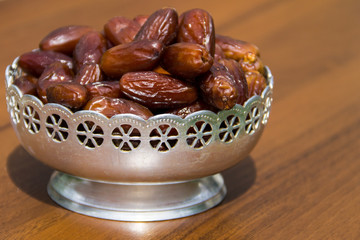 Dates fruit on a silver bowl on wooden table. The Muslim feast of the holy month of Ramadan Kareem