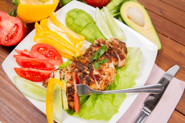 Chicken fillet with avocado and some vegetable on the side (tomato, cucumber, bell pepper) on a white background eaten with a fork