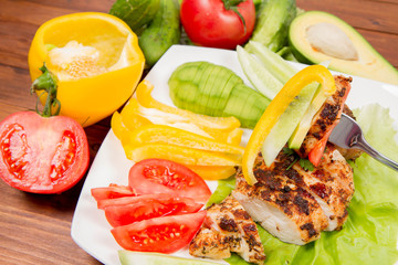 Chicken fillet with avocado and some vegetable on the side (tomato, cucumber, bell pepper) on a white background eaten with a fork